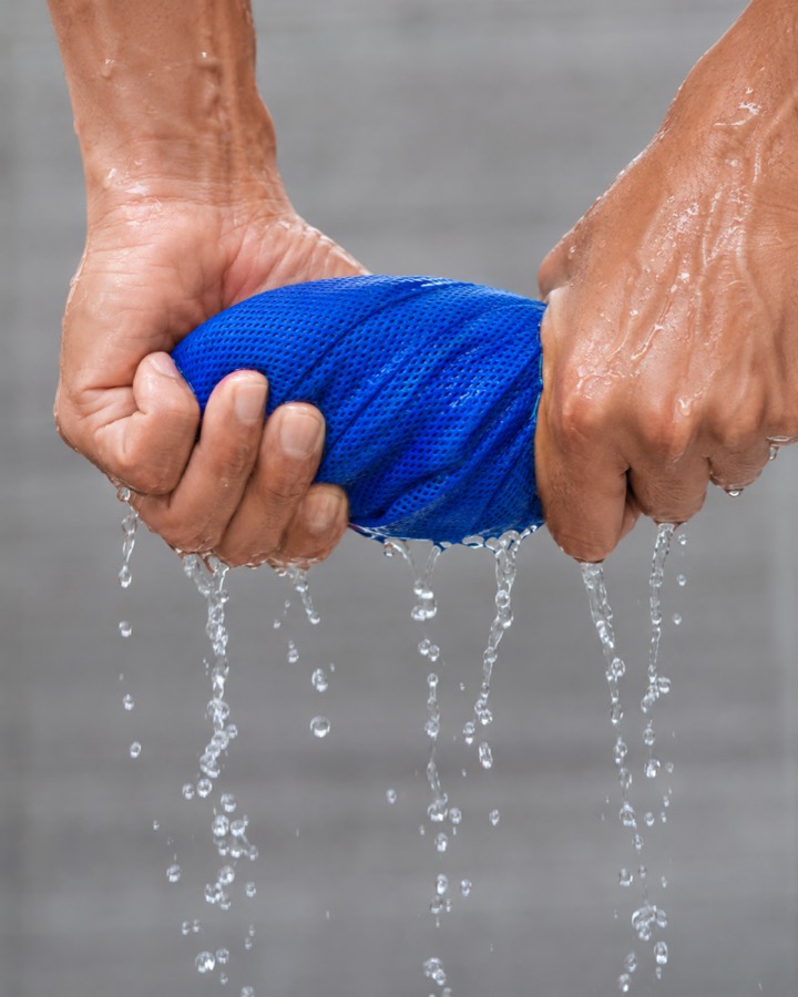 Two hands wringing water out of a blue cooling towel