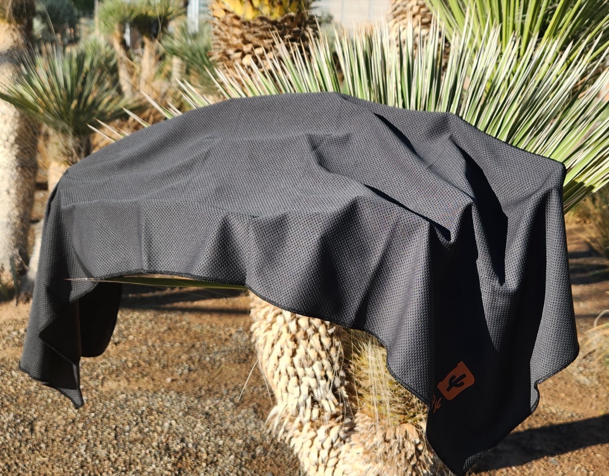 Two black Desert Towel cooling towels drying over a desert plant in the sun